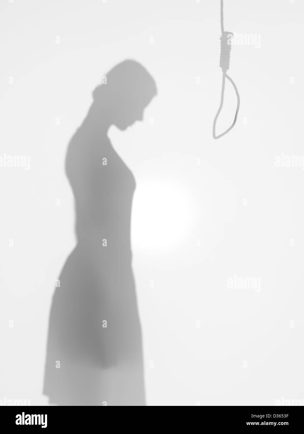 female body silhouette standing in front of a hanging rope committing suicide, behind a diffuse surface Stock Photo