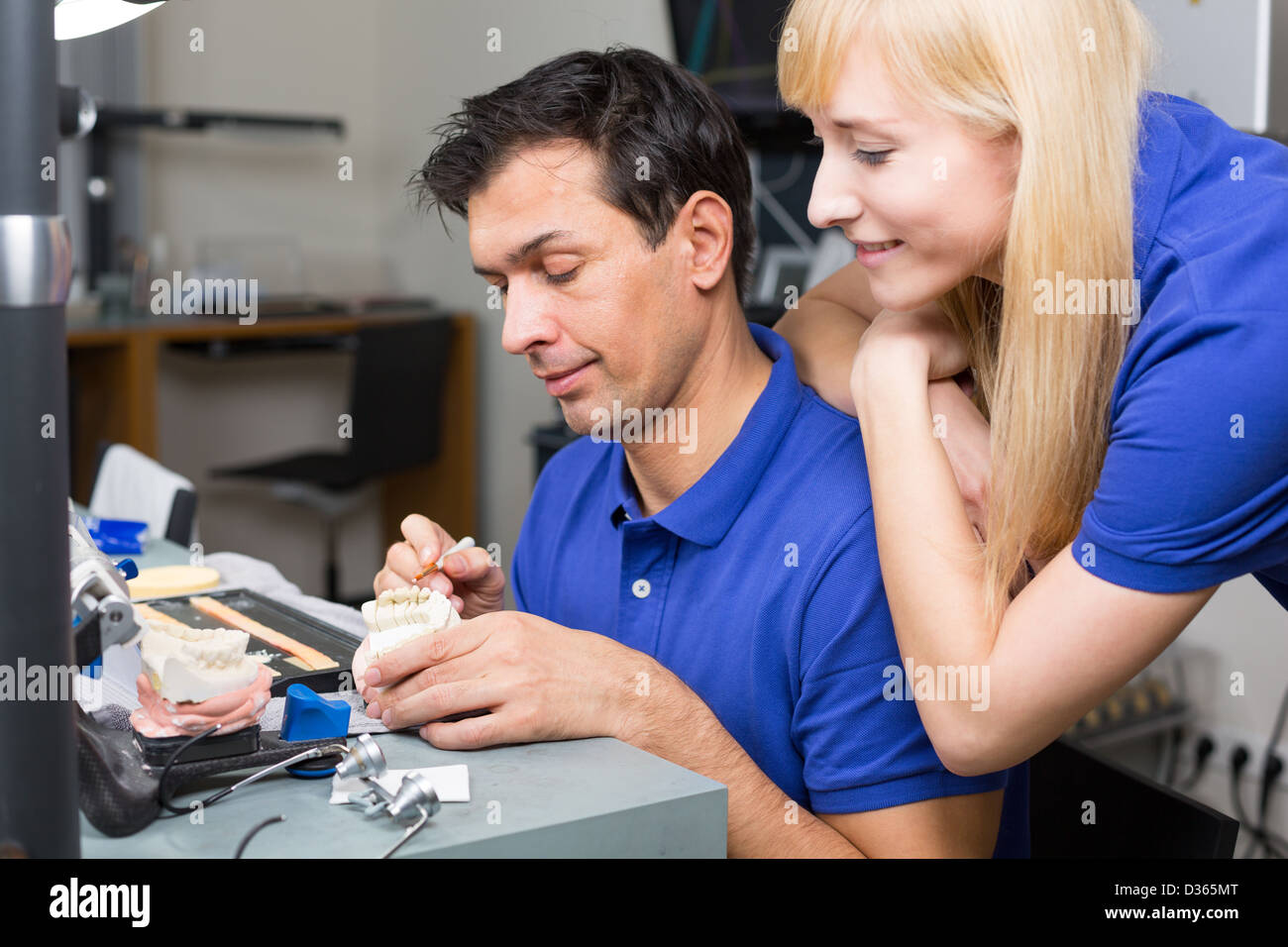 Woman watching dental technician applying porcelain to mold with a