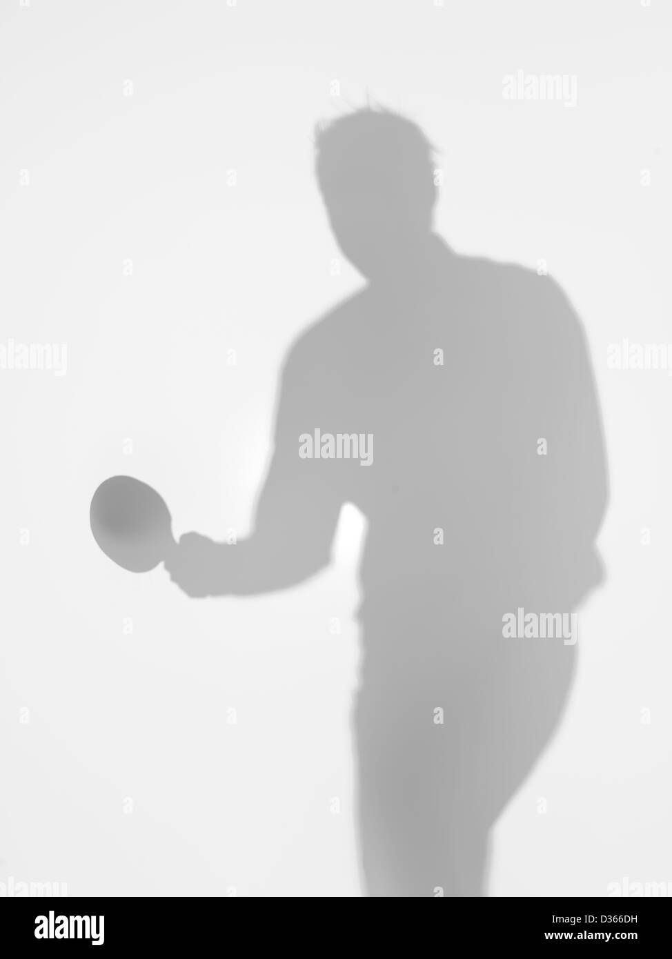male silhouette standing holding a table tennis racquet in one hand, behind a diffuse surface Stock Photo