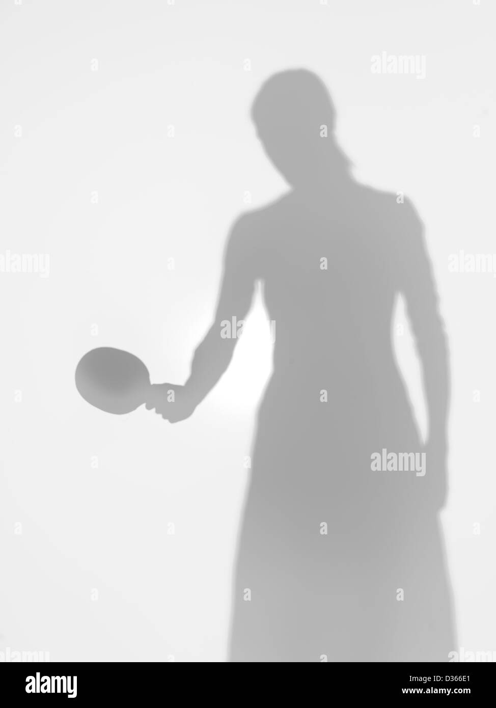 woman silhouette standing holding a table tennis racquet in one hand, behind a diffuse surface Stock Photo