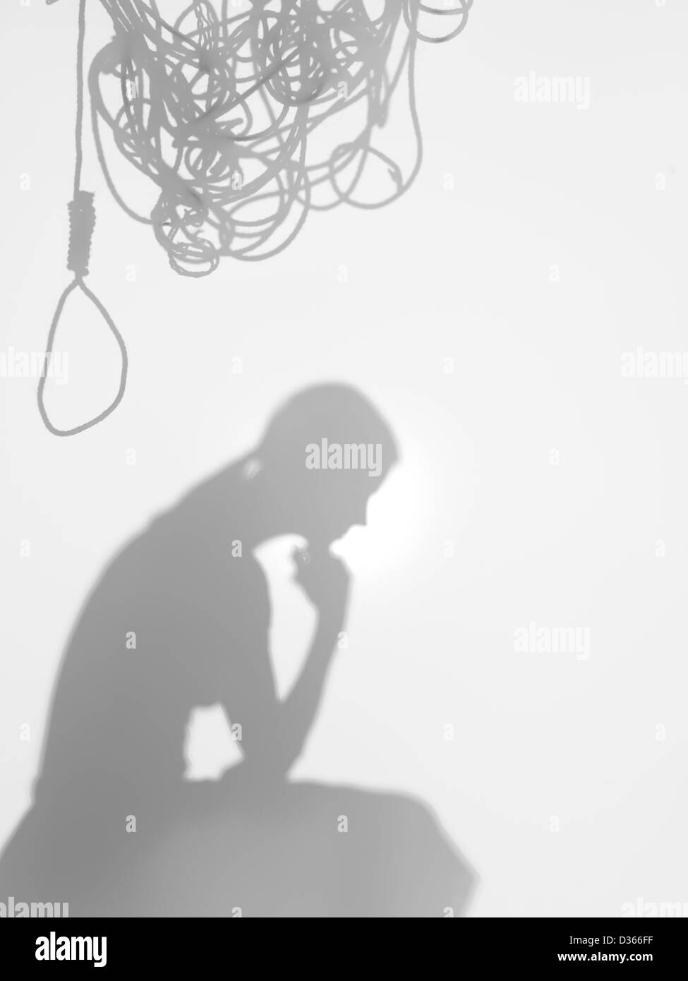 side view of woman sitting in a thinking posture with a tangled hanging rope on top of her head, behind a diffuse surface Stock Photo