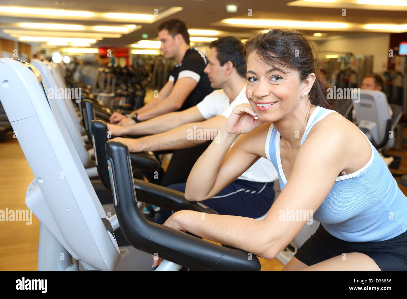 Two man and a woman on exercise bike smiling in the camera Stock Photo ...