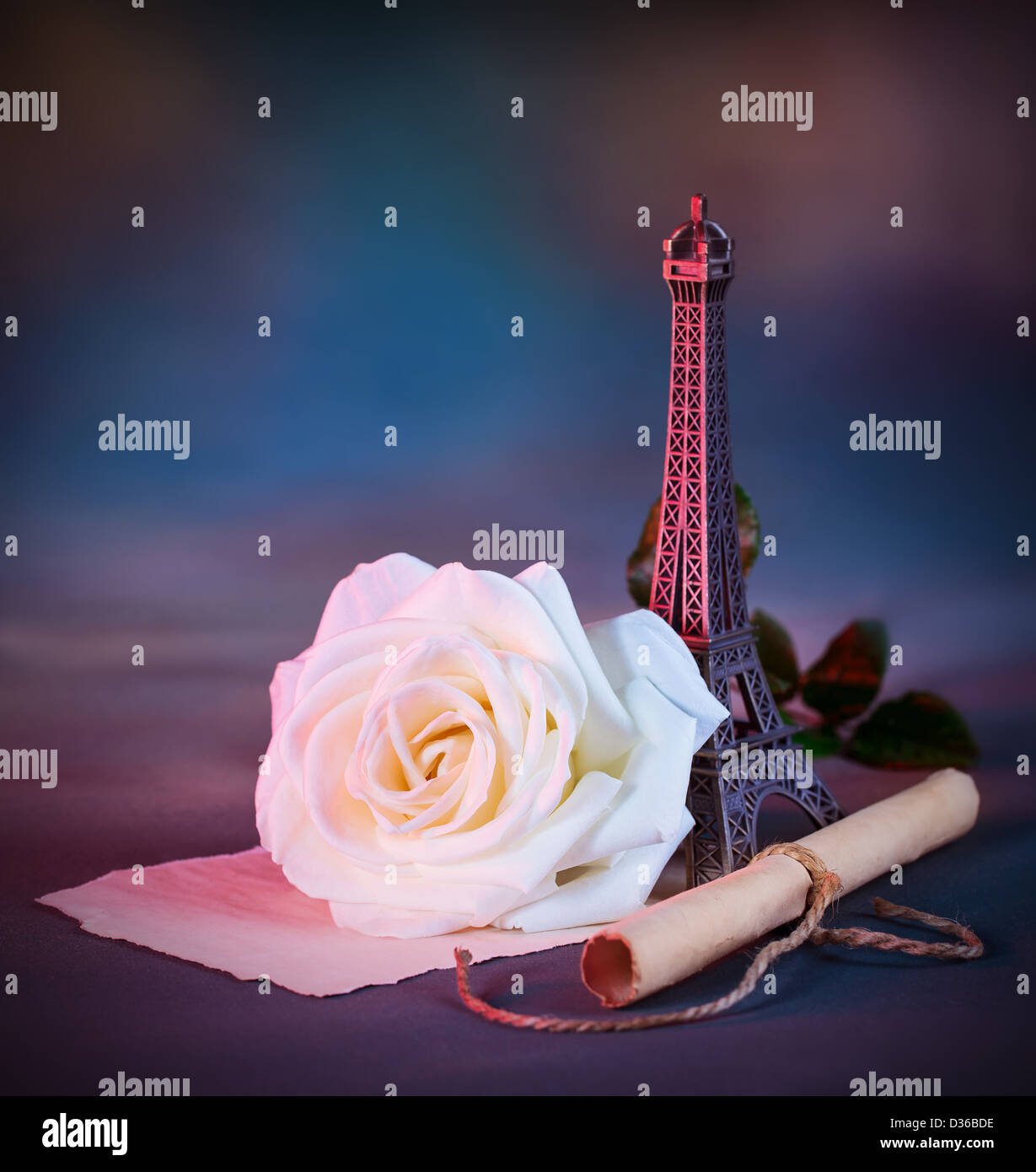 Picture of beautiful retro style still life over blue grunge background, white fresh rose flower, small decorative Eiffel tower Stock Photo