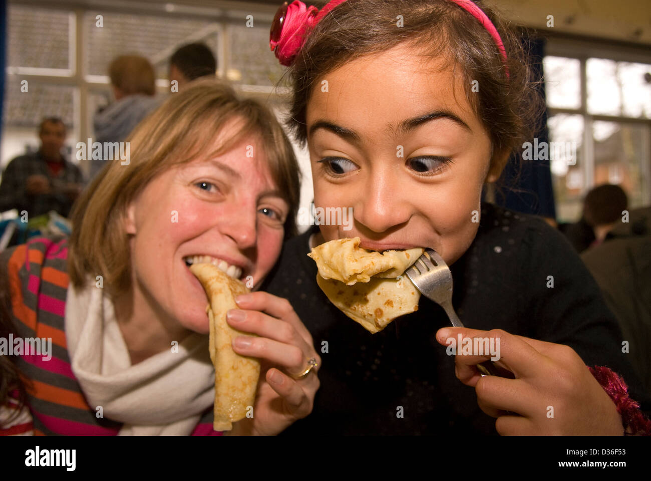 7 year old girl with her mum in background eating pancakes in local village hall celebrating Shrove Tuesday Stock Photo
