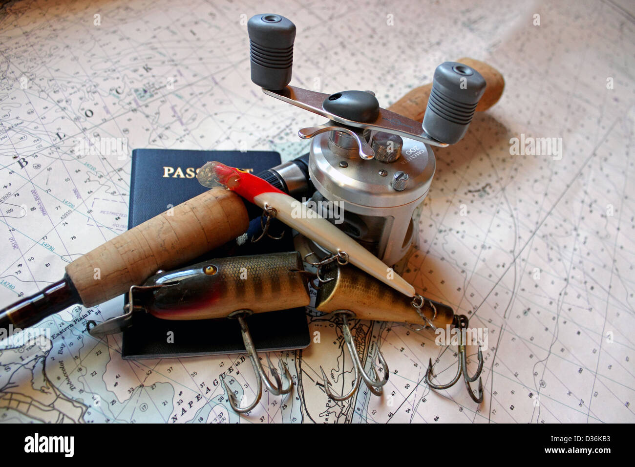 A fishing rod and lures with a passport rest on a nautical chart. Stock Photo