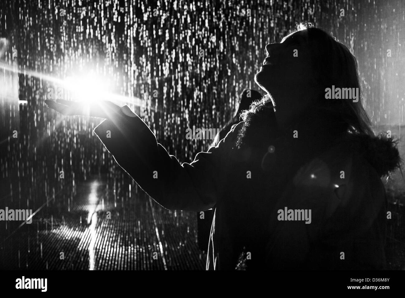 Silhouette of Woman standing in rain with light coming from hand Stock Photo