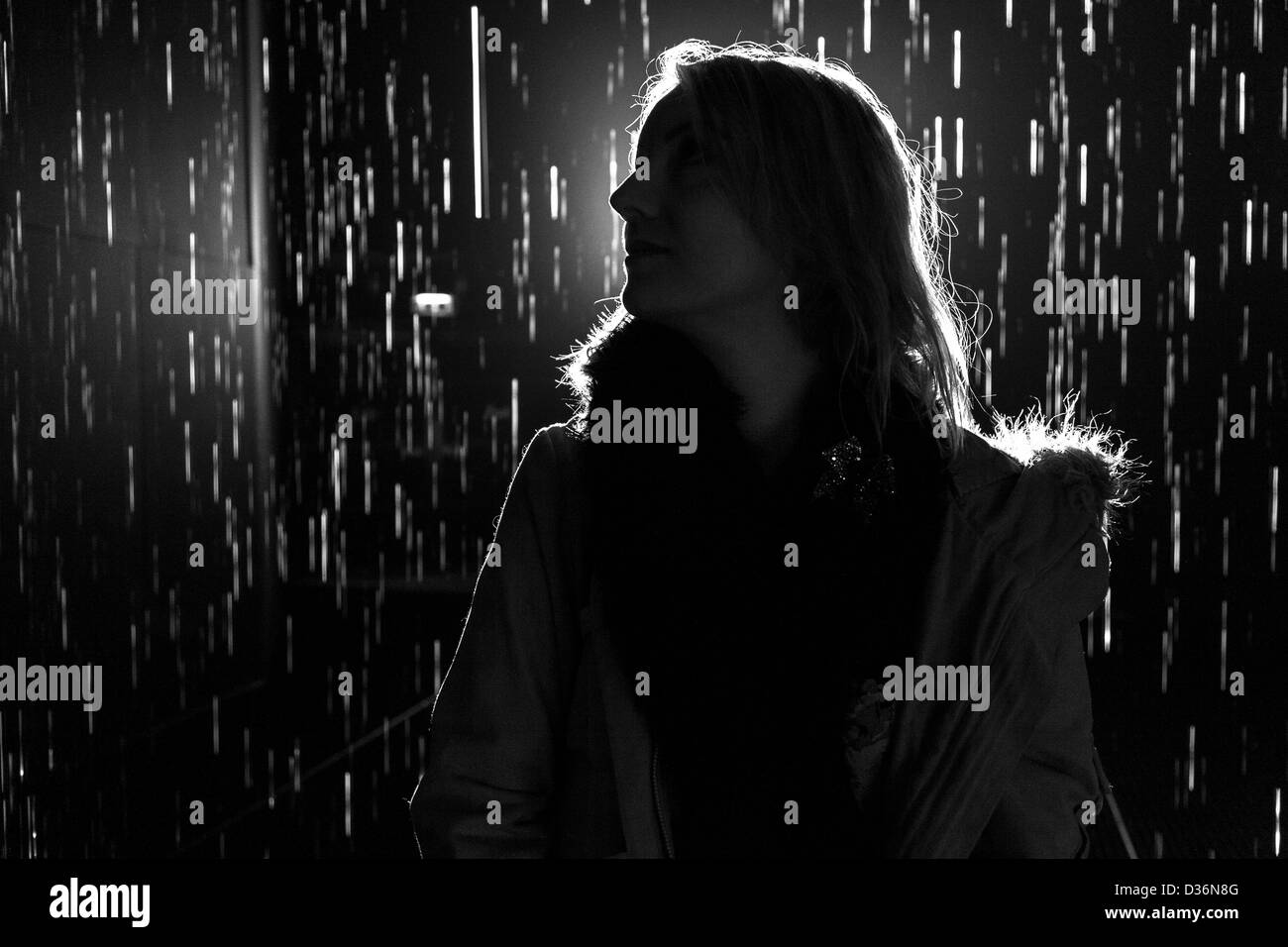 black and white Silhouette of woman looking to the side in the rain with light coming from behind. Stock Photo