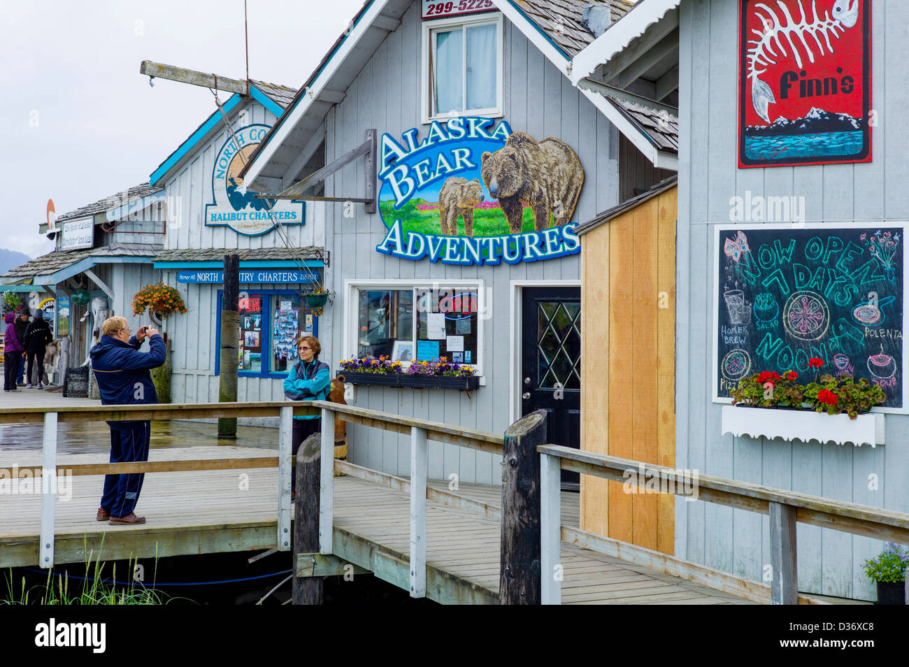 Tourists photograph each other in front of gift shops, stores and restaurants along the Homer Spit, Homer, Alaska, USA Stock Photo