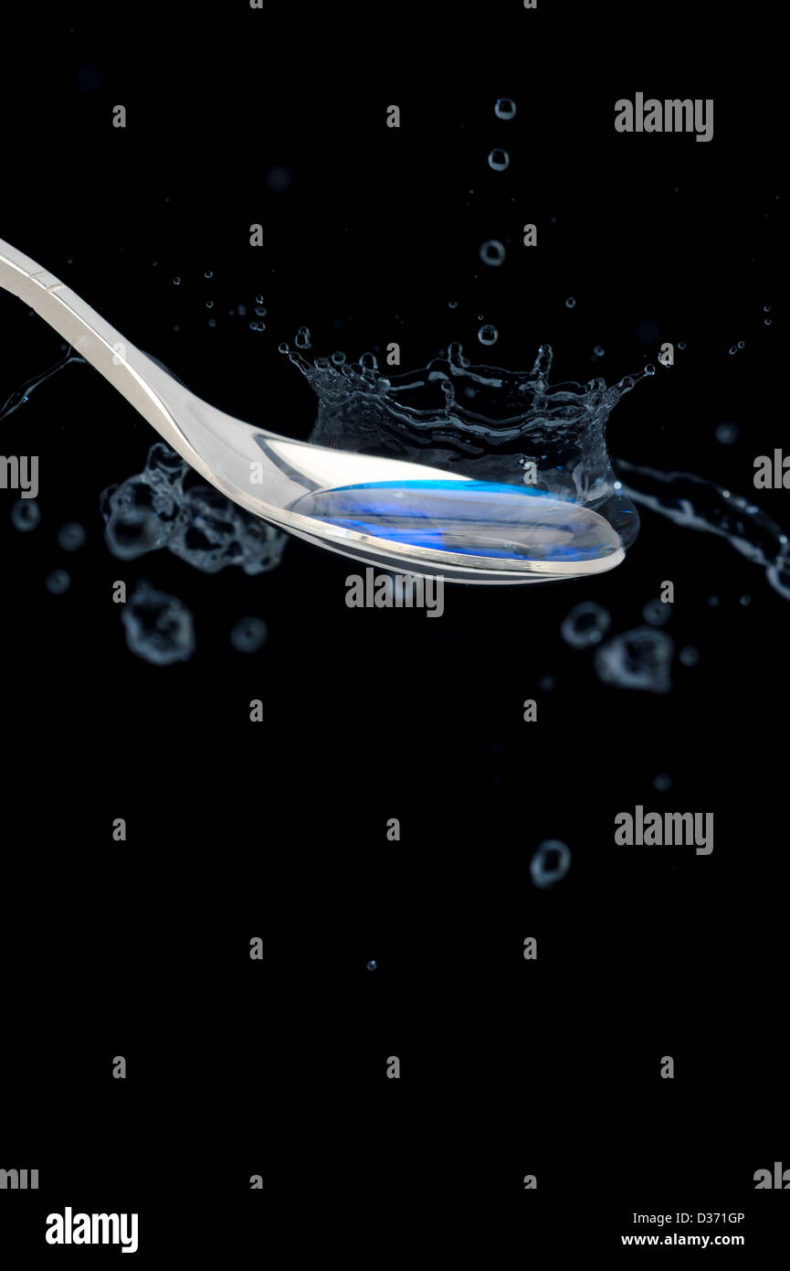 Teaspoon with dripping blue liquid water drops in black background