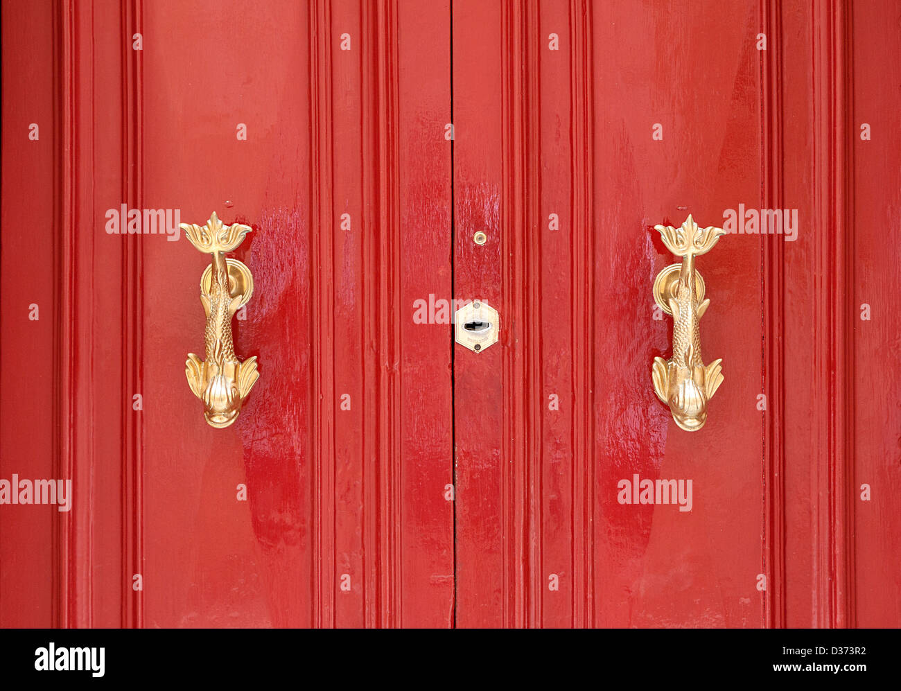 Two brass door knockers in the shape of fish on a bright red door. Stock Photo