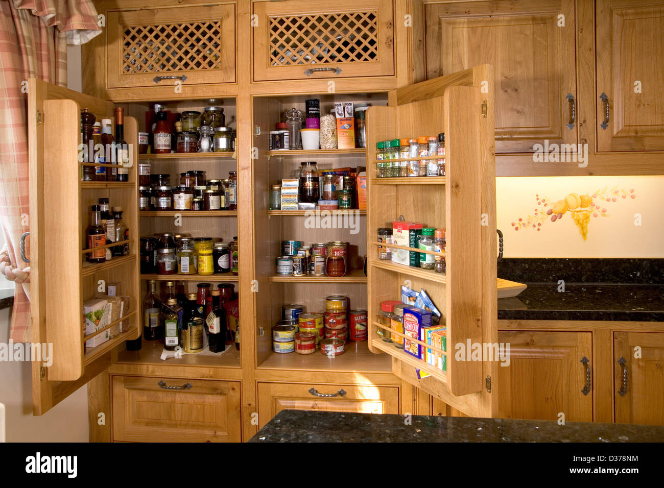 Well stocked cupboards in an upmarket solid wood fitted kitchen. Stock Photo