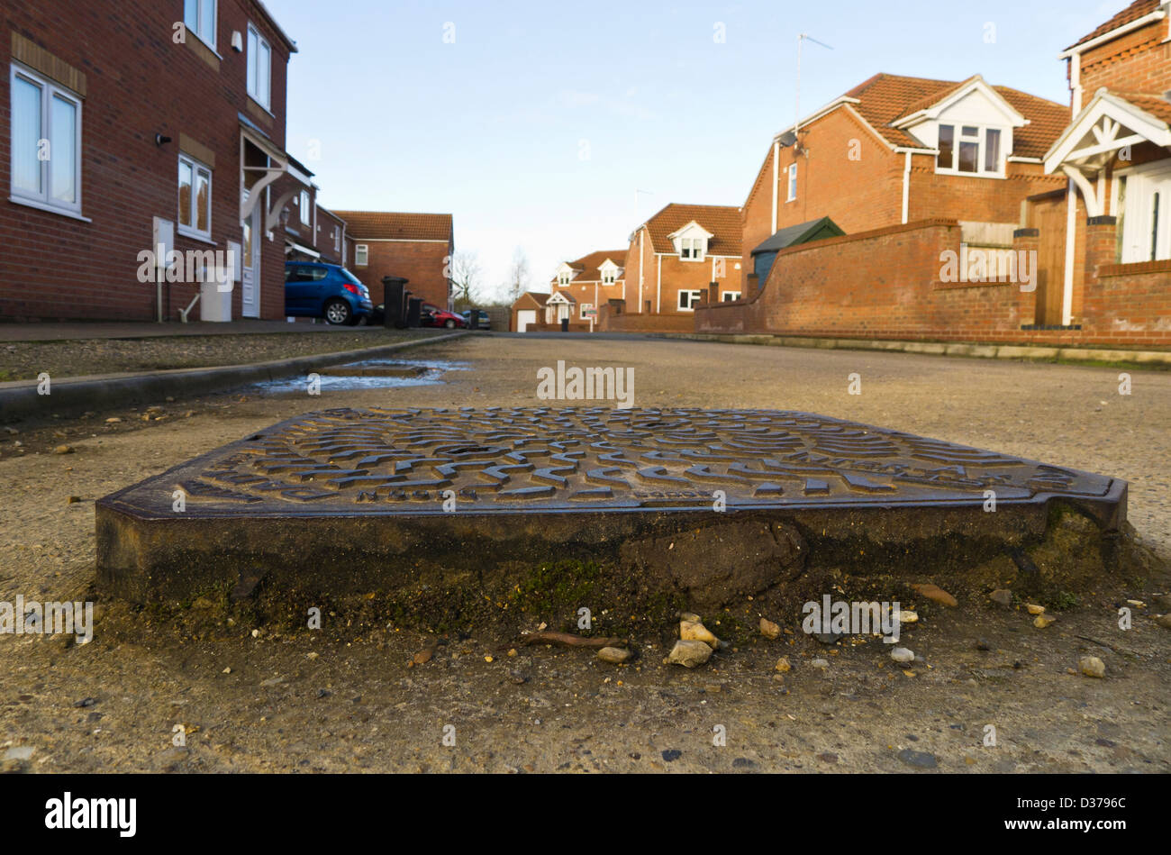 A raised manhole cover on a poorly surfaced road in King's Lynn, Norfolk. Stock Photo
