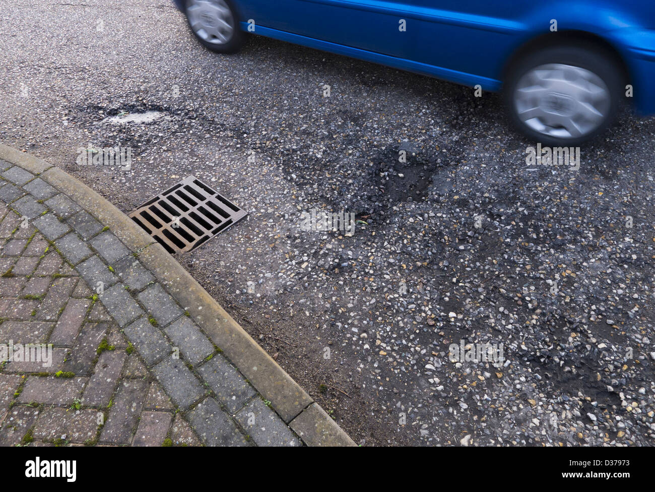 Car driving past potholes and a crumbling road surface. Stock Photo
