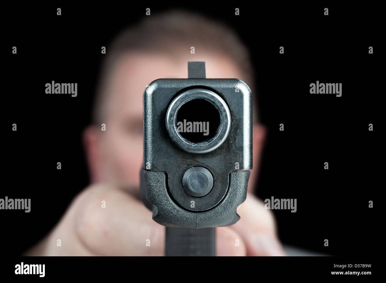 A man aims his semi automatic pistol. Selectively focused on the front of the gun. Stock Photo