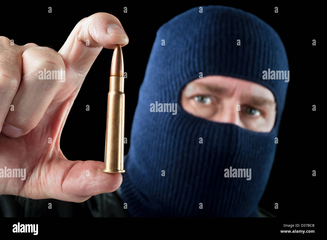 A terrorist wearing a ski mask as a disguise holds out a large automatic rifle bullet. Stock Photo