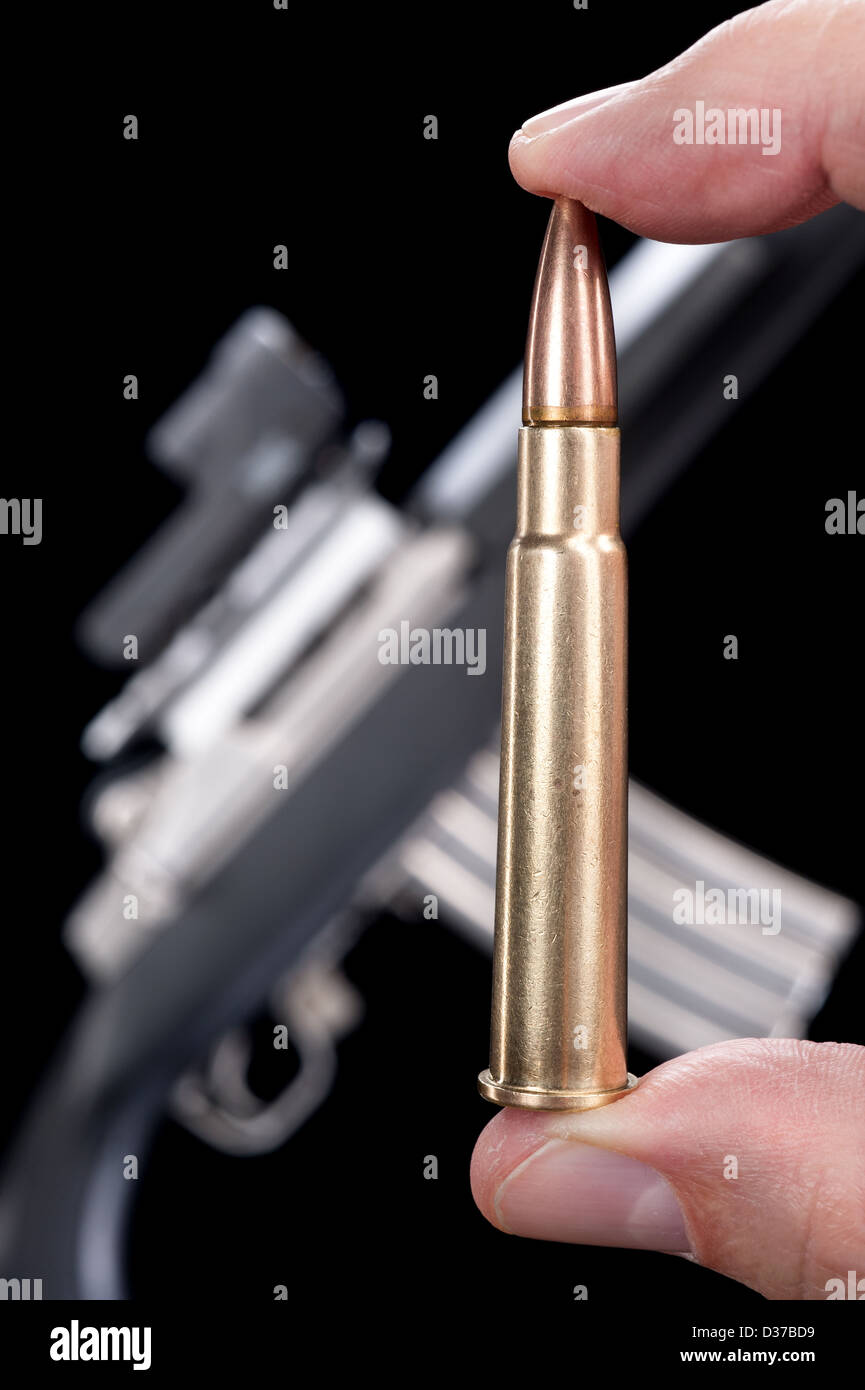 A man holds a high powered bullet in front of an automatic machine gun. Stock Photo