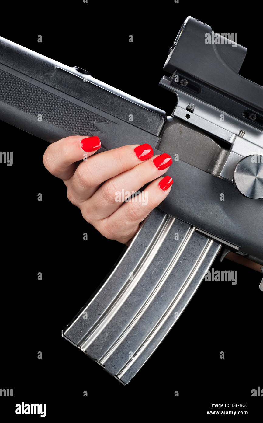 A woman with pretty red painted fingernails holds onto an assault rifle with a fully loaded magazine. Stock Photo