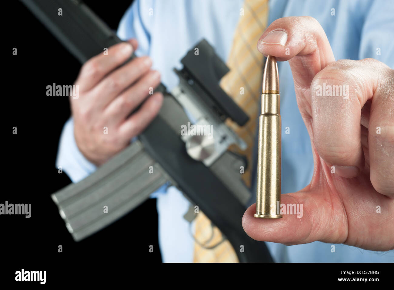 A businessman shows a large 223 bullet for his automatic assault rifle. Stock Photo