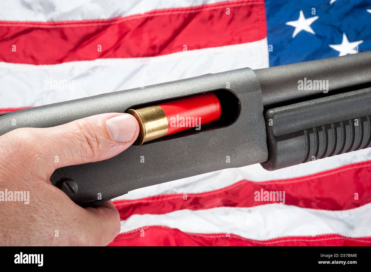 A man loads a shotgun shell into a pump action shotgun. Shot against an American flag. Stock Photo