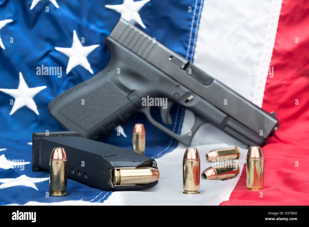 A handgun with a full magazine and scattered bullets on an American flag. Stock Photo