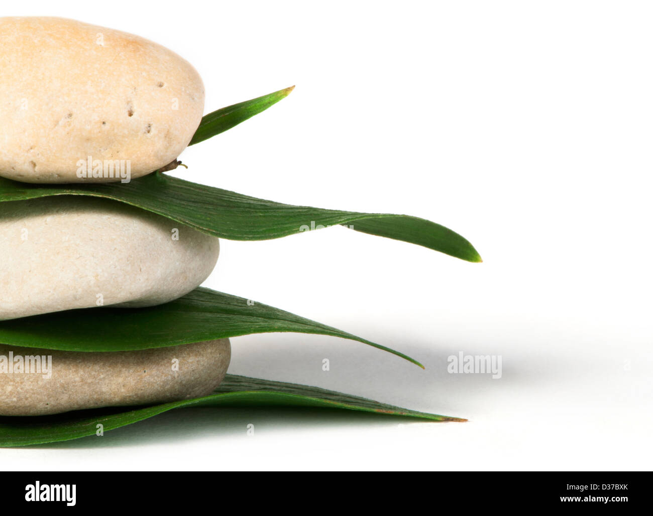 Stacked stones on base of green leafs. White isolated studio shot. Stock Photo