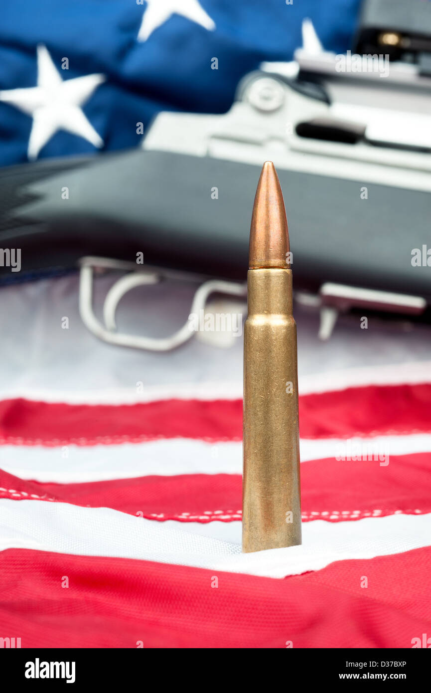 A single bullet in front of an assault rifle sitting on an American flag. Stock Photo