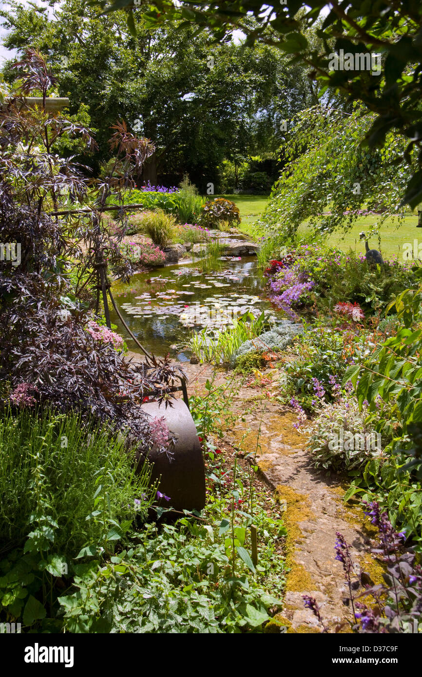 UK gardens. A large garden pond in a mature garden with an old lawn roller feature.. Stock Photo