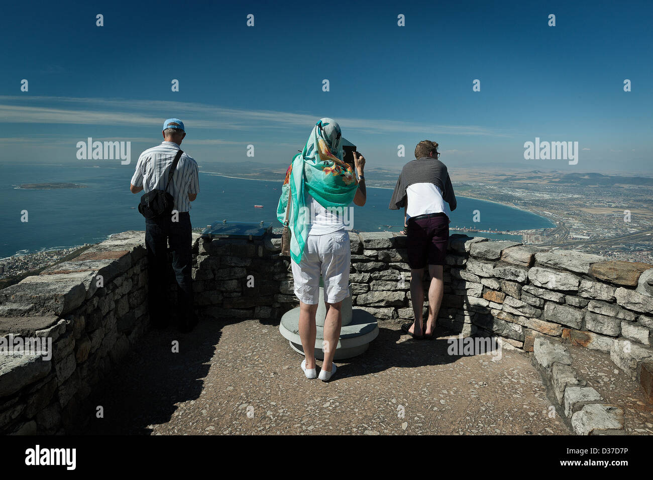 Three tourists enjoy the view from the top of Table Mountains look out point from where the ocean, harbour and CBD can be seen. Stock Photo