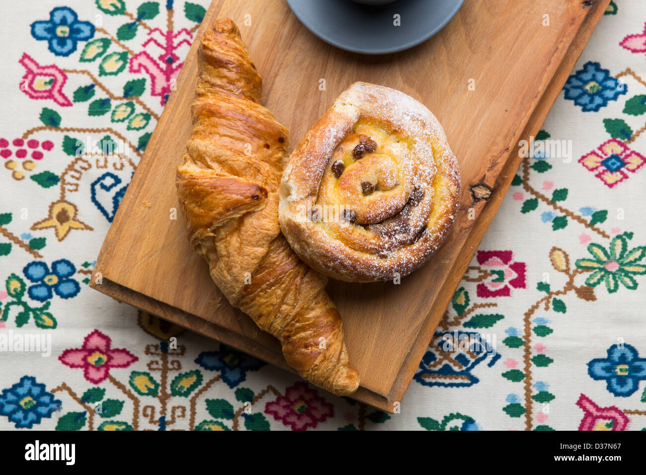 Pastries and coffee on a natural wood chopping board on Danish folk fabric lit from the top of the frame. Stock Photo