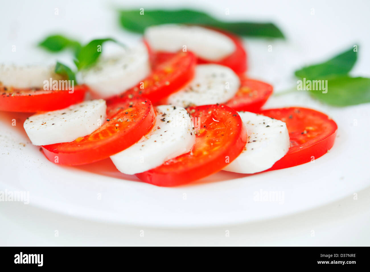 Tomato and mozzarella with basil leaves on a plate Stock Photo - Alamy