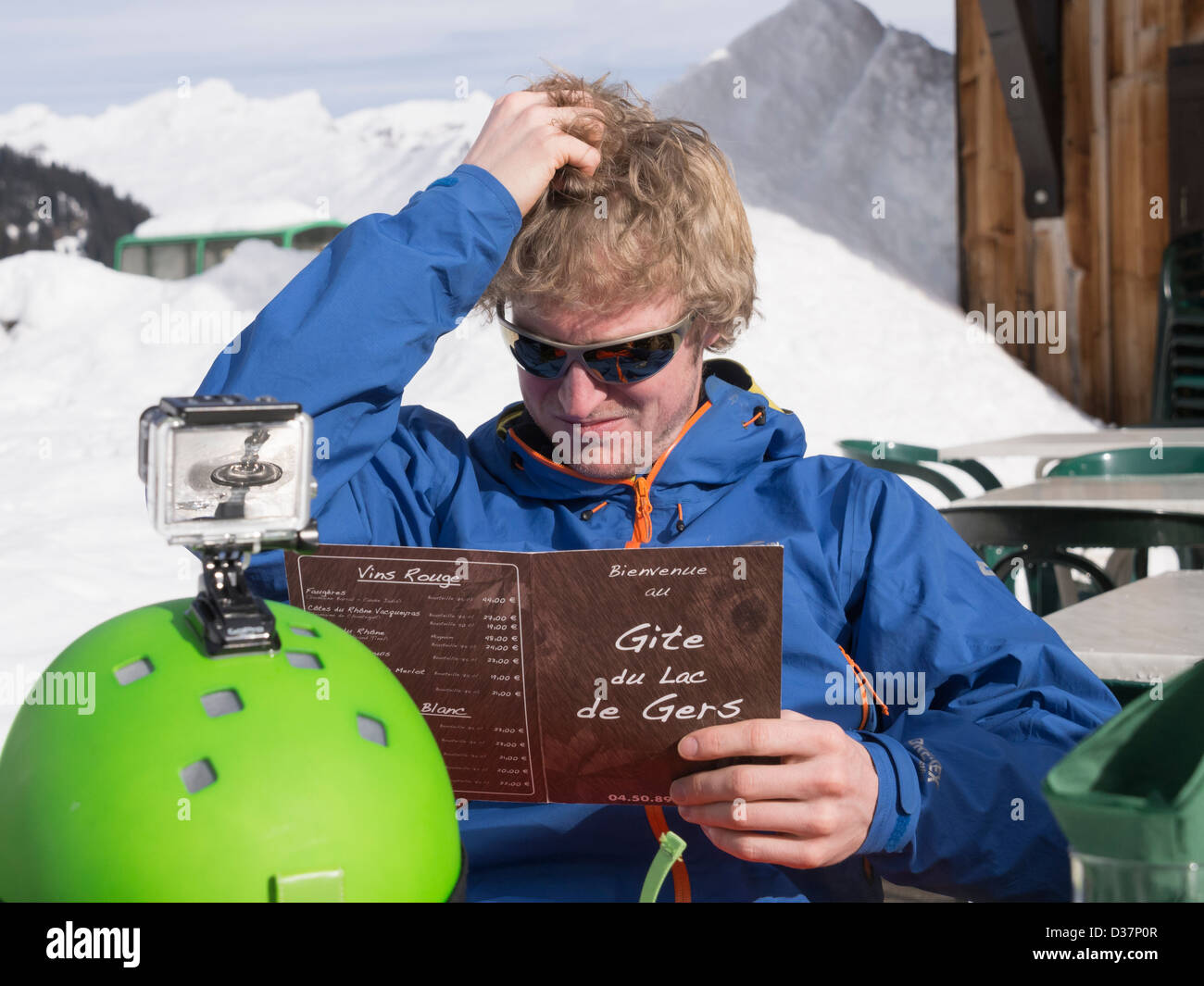 Man thinking scratching his head whilst trying to decide what to eat from a menu outside Gite du Lac de Gers ski restaurant in winter. Samoens France Stock Photo
