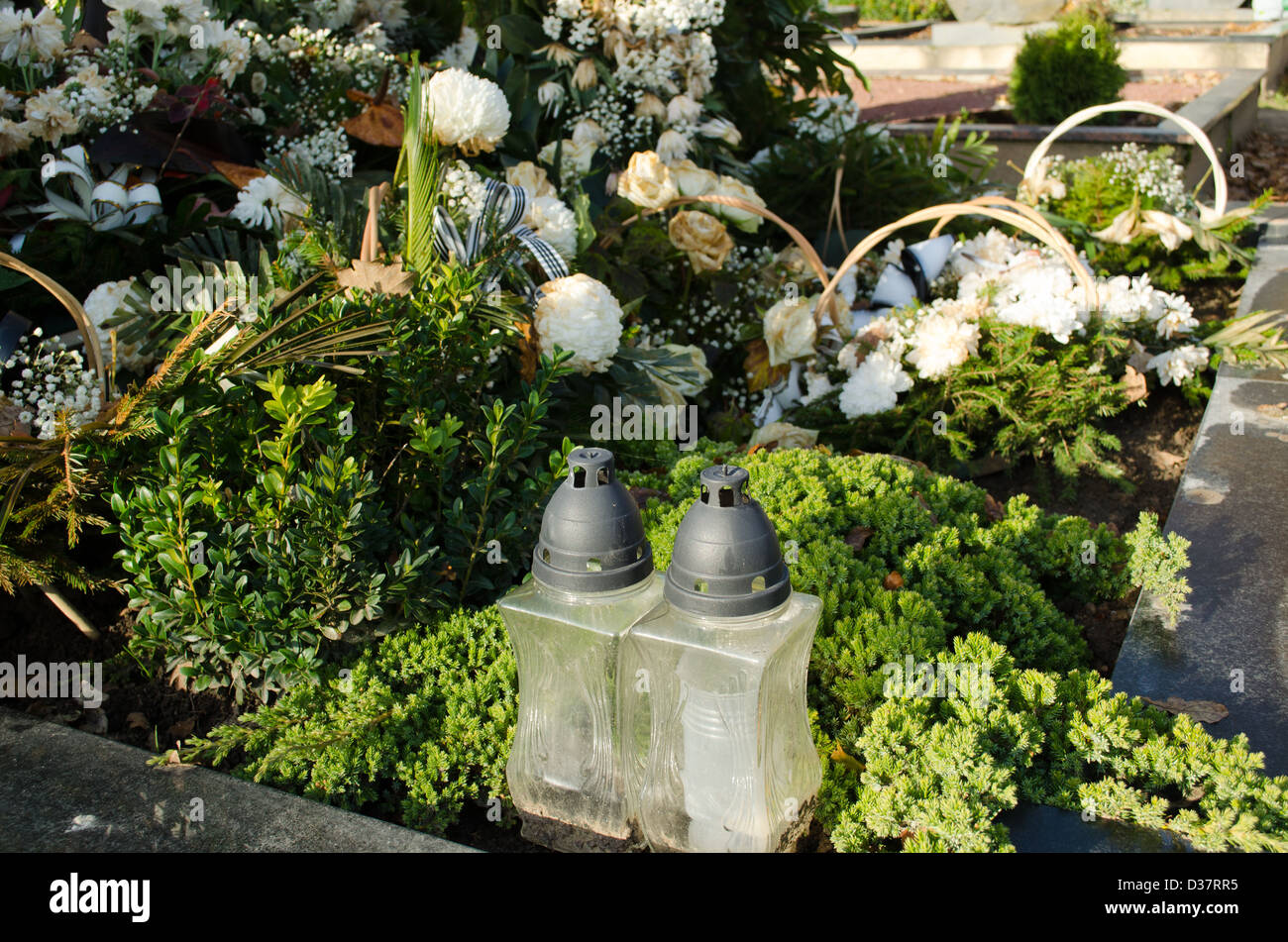 new grave tomb candle glass box and many flower pot crown wreath in cemetery. Stock Photo