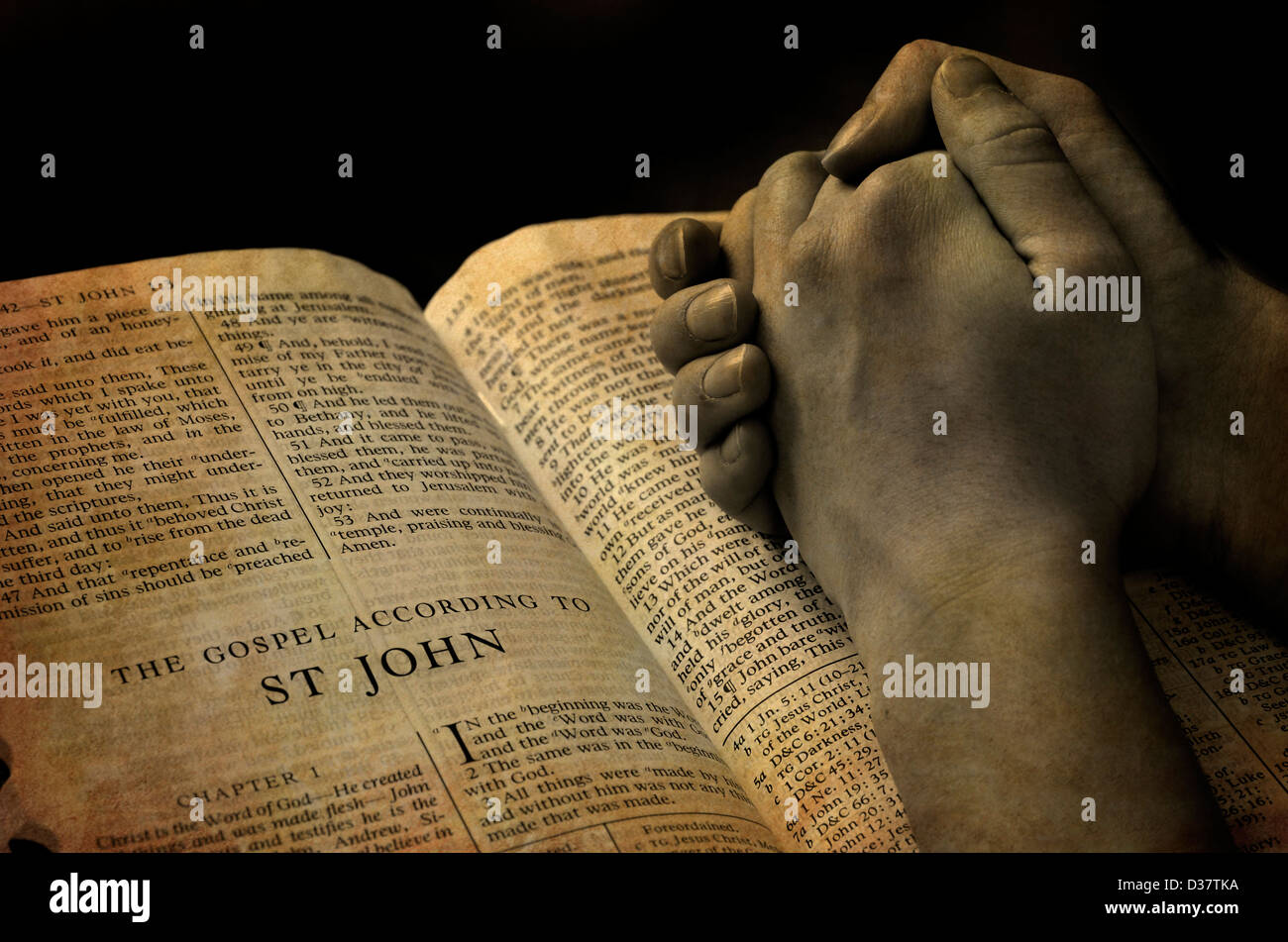 Hands of a person raised together in prayer with bible Stock Photo