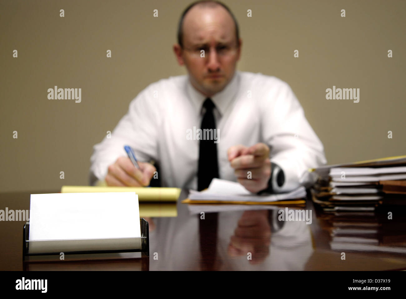 Stern Man sitting at desk holding pen and pointing finger at viewer