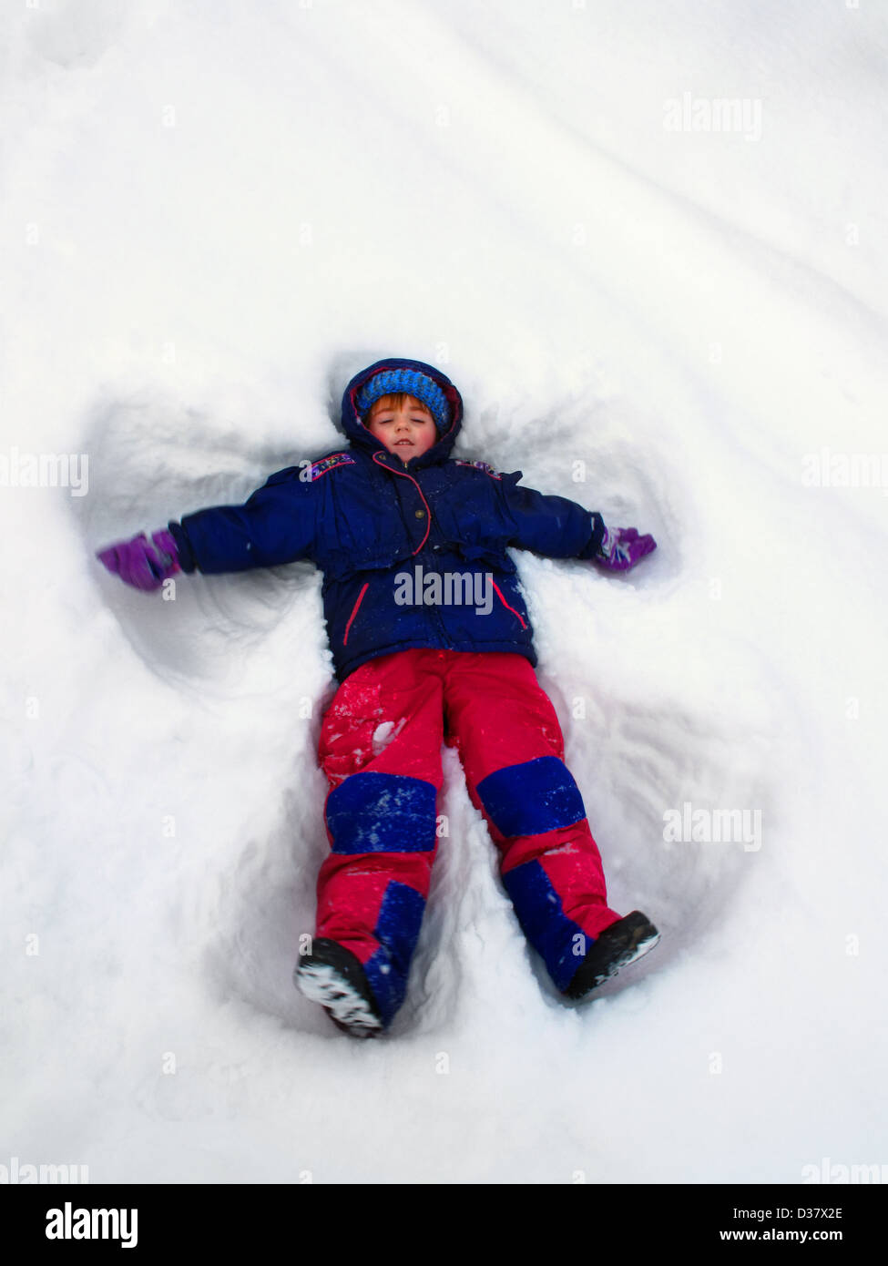 Child playing in the winter making a snow angel Stock Photo