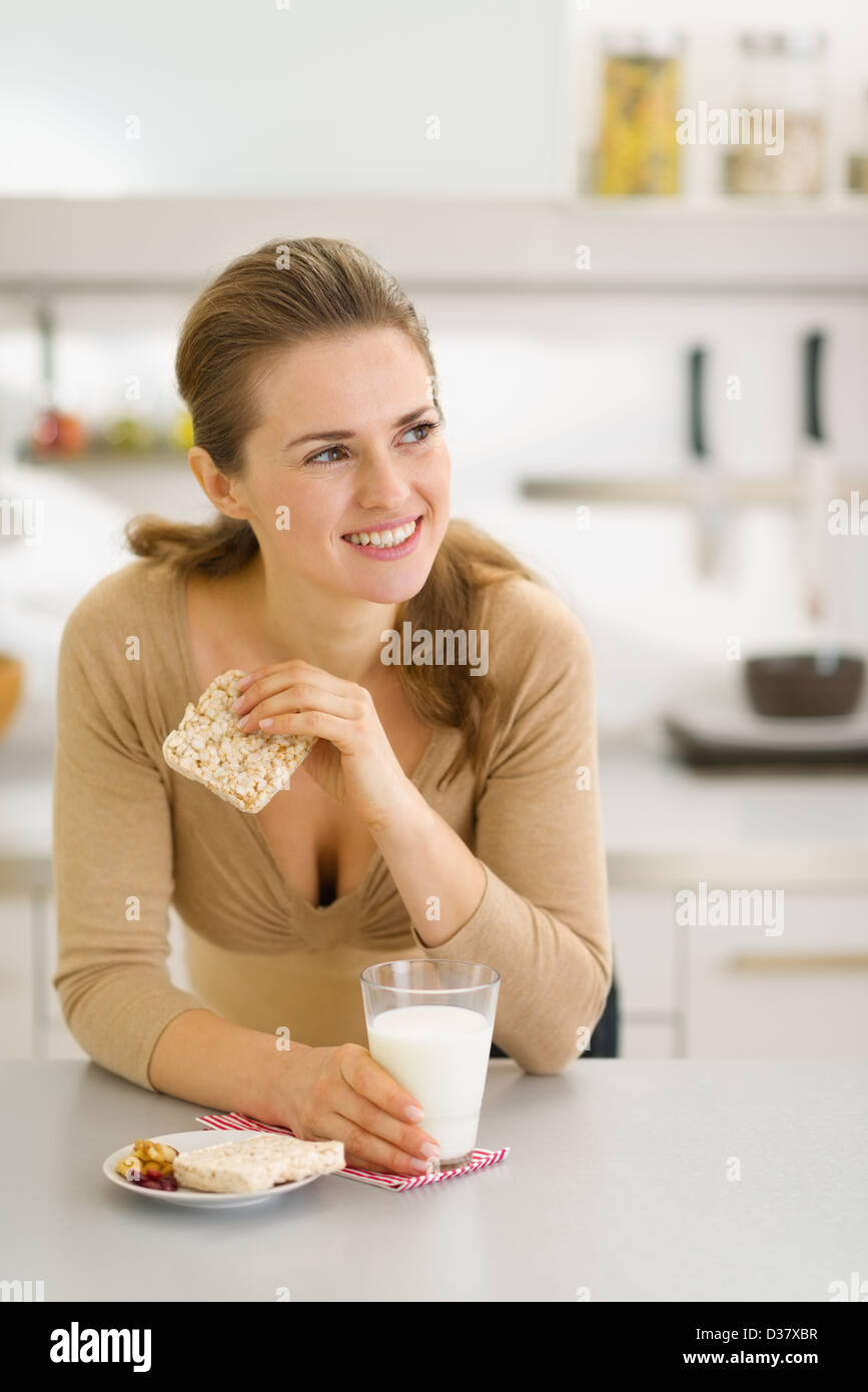 Young woman eating snacks in modern kitchen and looking on copy space