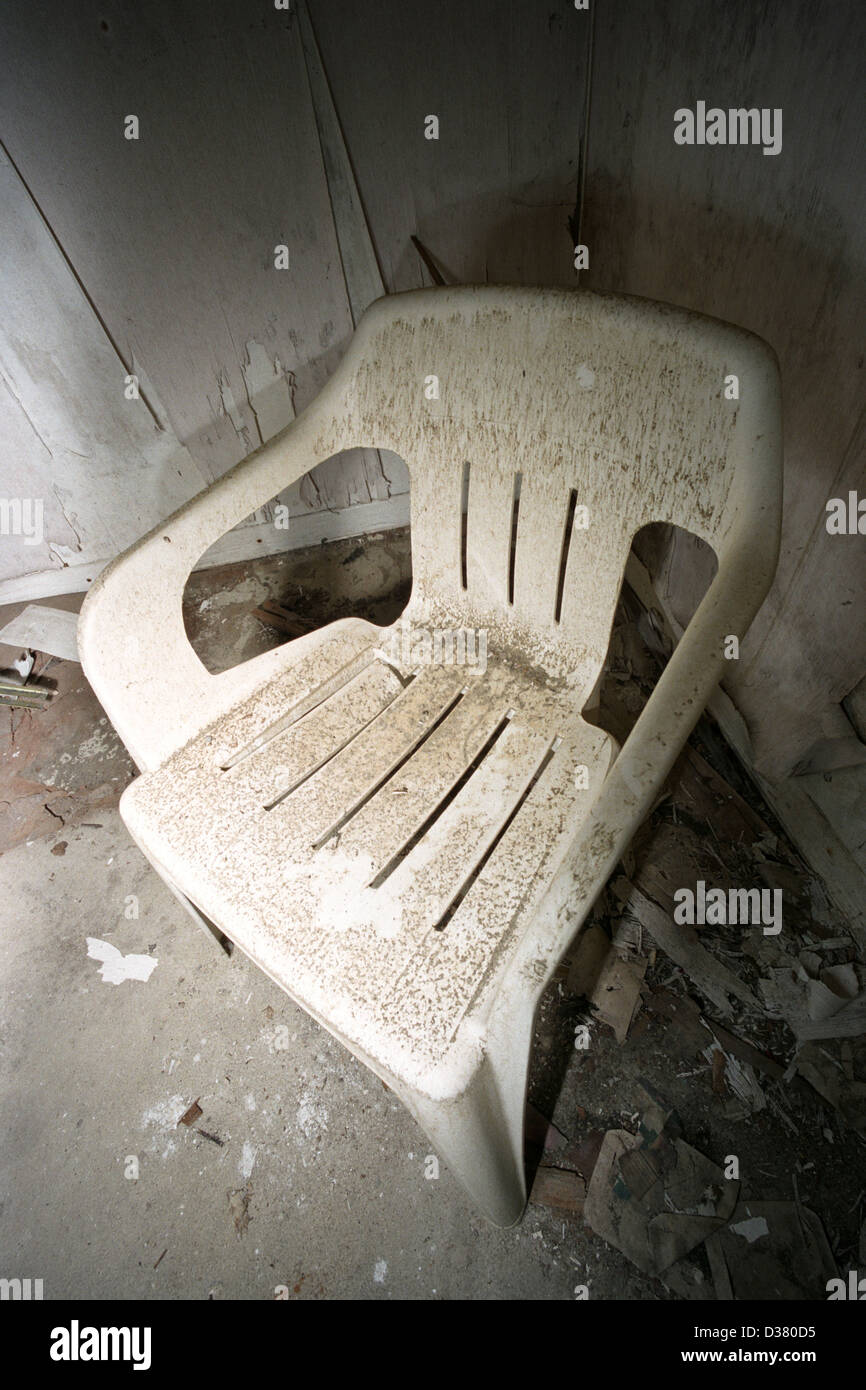 A dirty white plastic chair in the corner of a derelict room on a