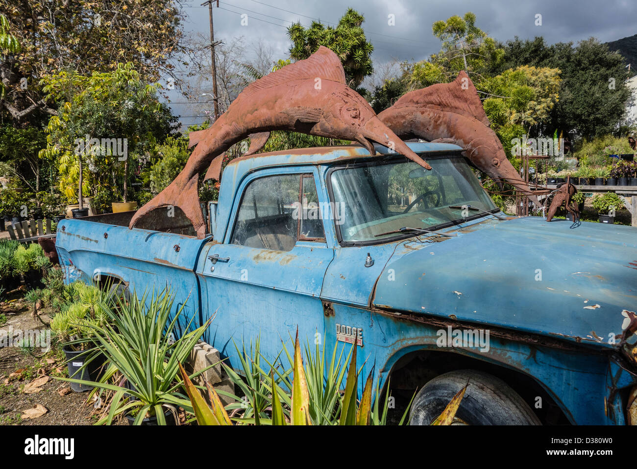Two large rusted steel dolphin sculptures sit atop an old blue Dodge pickup truck that is no longer in service. Stock Photo