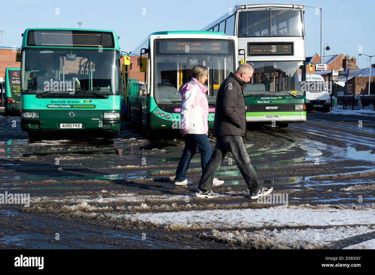 Two people walking across King's Lynn bus station with snow on the ground. Stock Photo