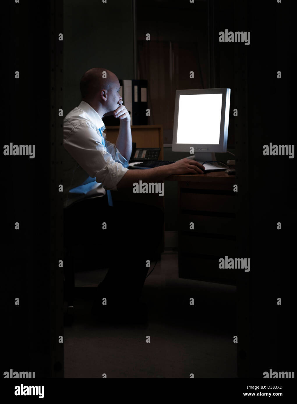 Late night office worker working overtime. White collar worker working on computer at night in dark office. Stock Photo