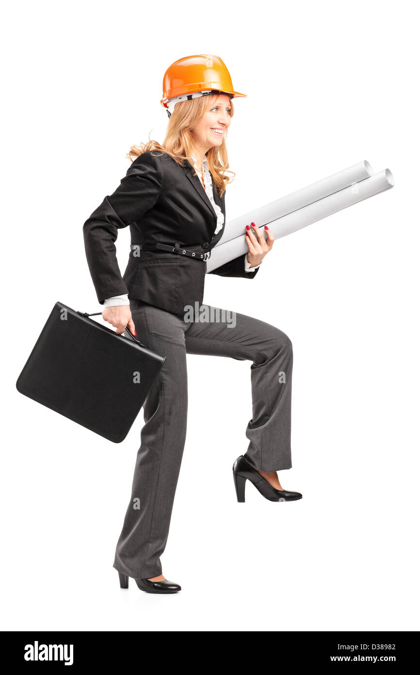 Full length portrait of a mature female architect with helmet holding blueprints and suitcase, walking with big steps isolated o Stock Photo