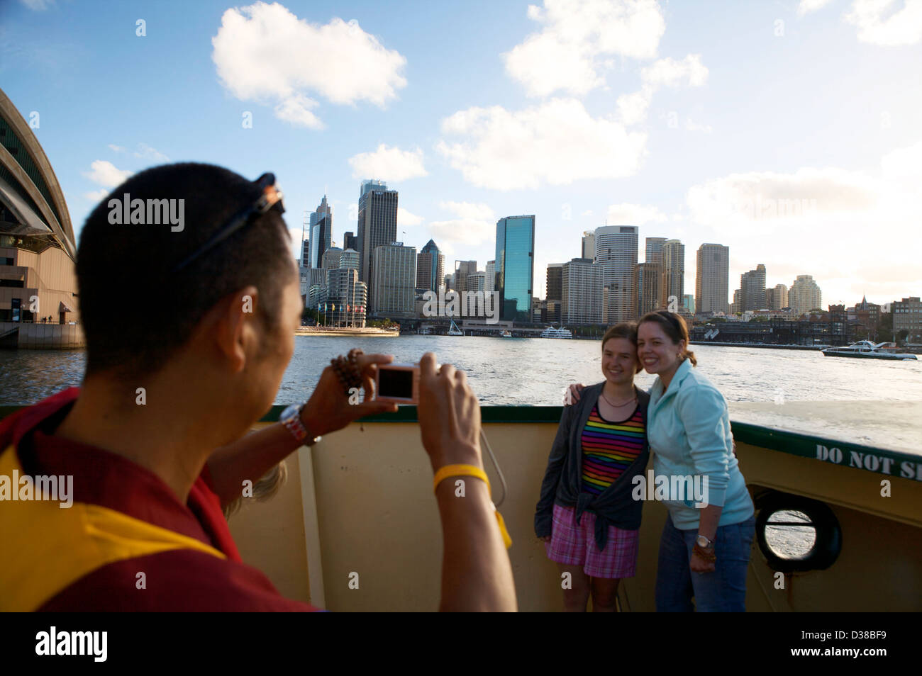 A Buddist monk takes a picture of two girls with the Sydney skyline behind them using a small digital camera. Stock Photo