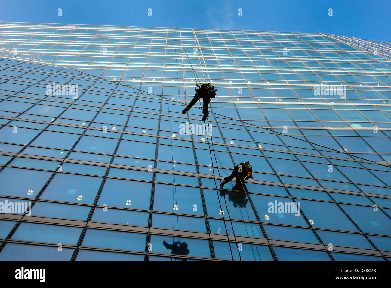 Two men abseil while cleaning windows of a large glass office block Stock Photo