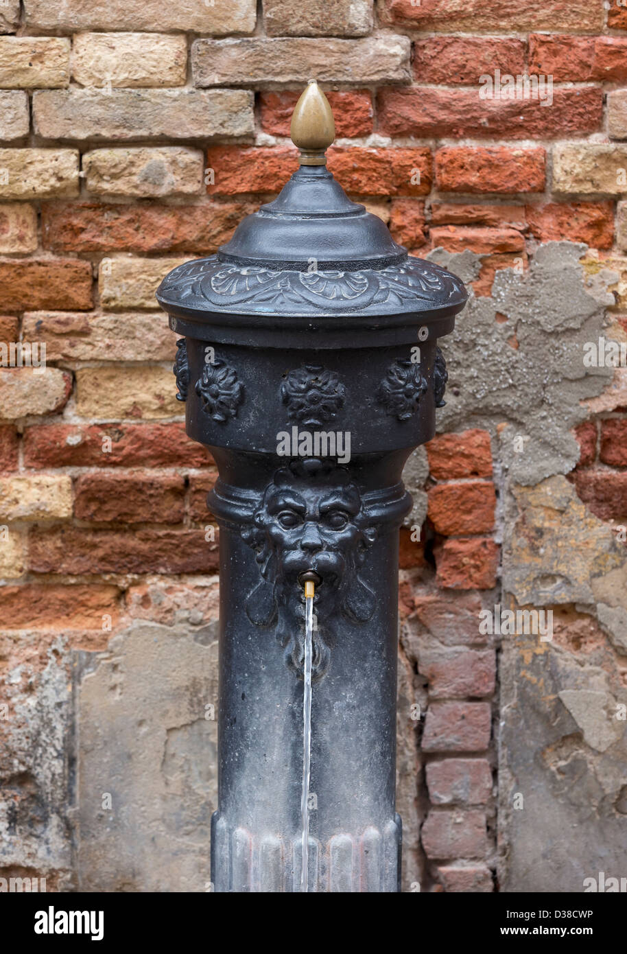 A cast iron public drinking fountain with the figure of a lions head gushing water from its mouth in Venice Stock Photo