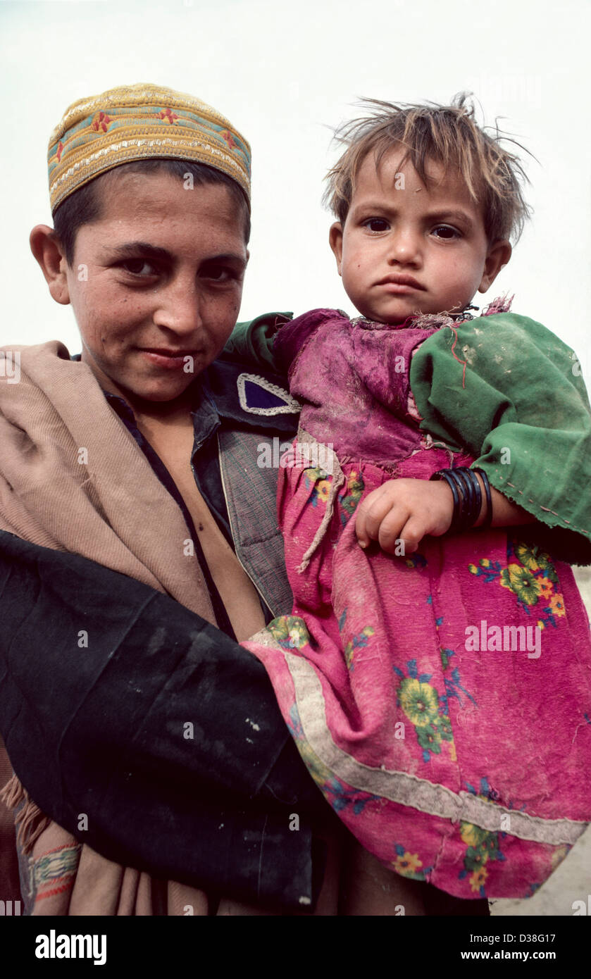 Portrait of an Afghan refugee boy carrying his little sister in a refugee camp. Peshawar, Pakistan Stock Photo