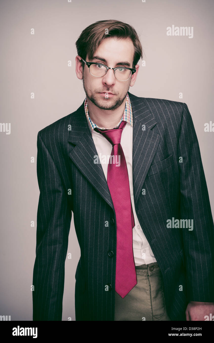 Businessman in his 20s wearing pinstripe suit jacket, white shirt, red tie and glasses looks unimpressedly to camera. Stock Photo