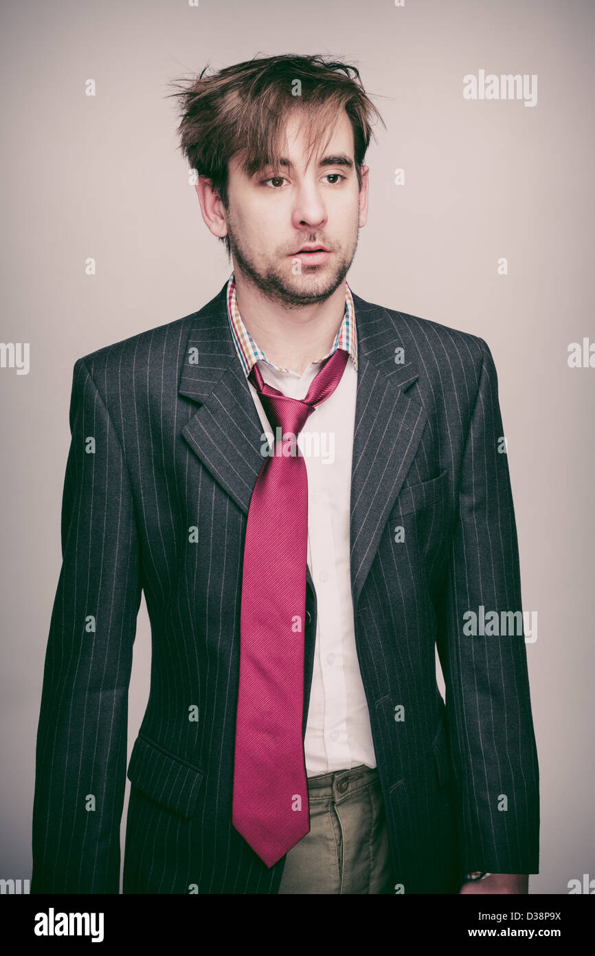 Businessman in his 20s wearing pinstripe suit jacket, white shirt, loose red tie, looks stunned. Stock Photo