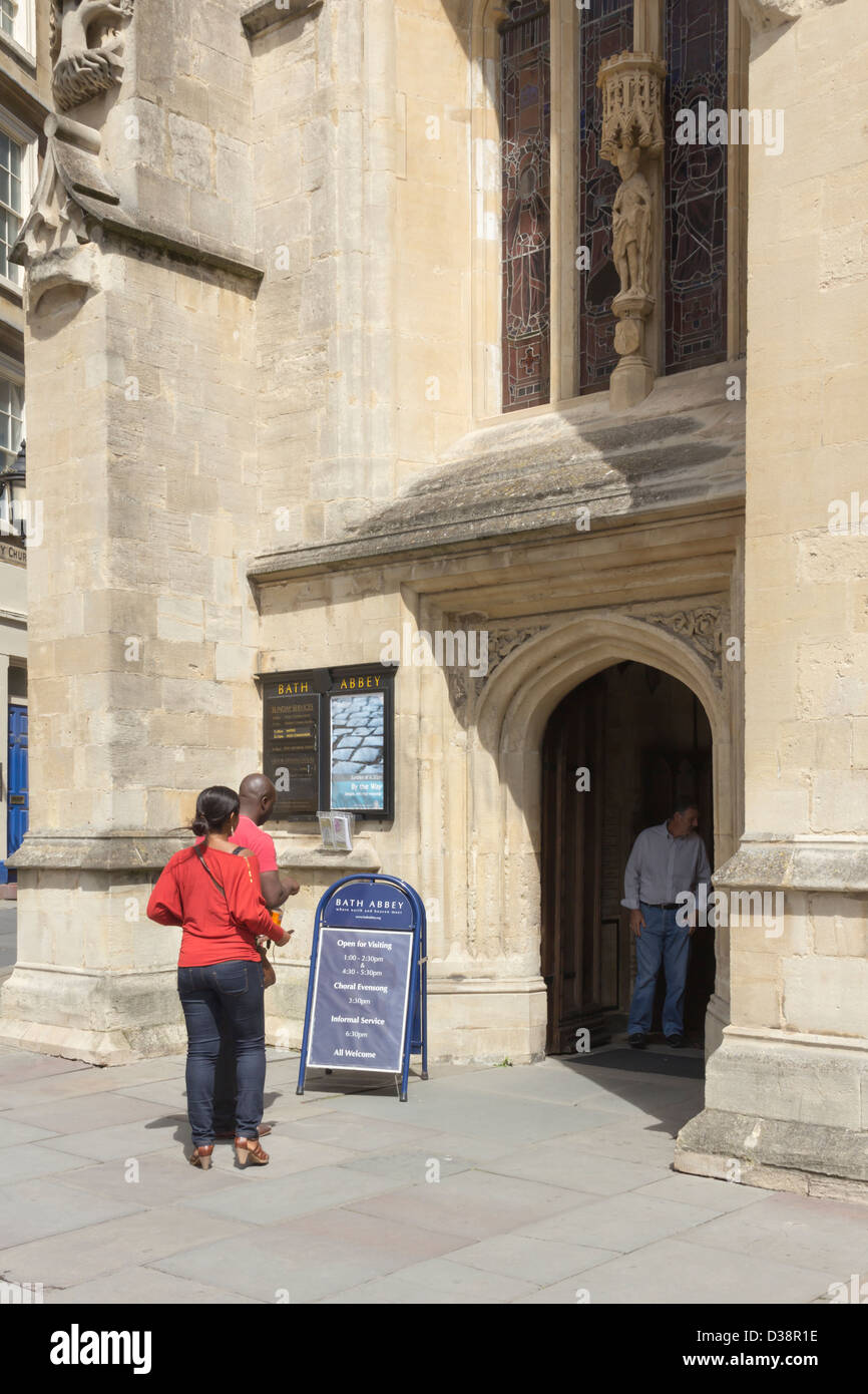 Entrance to Bath Abbey with two visitors reading the information board and another stood in the doorway. Stock Photo