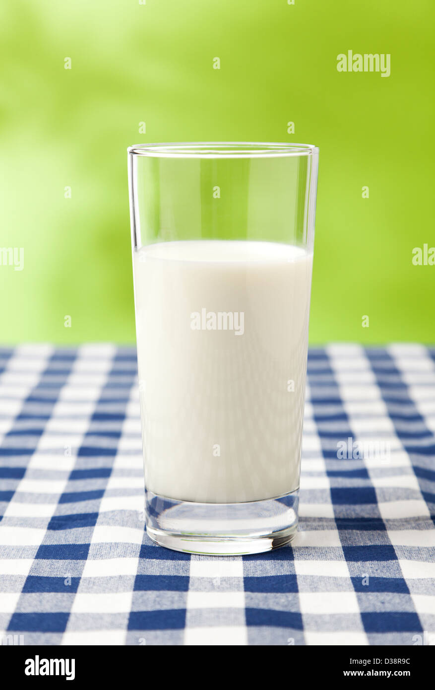 Glass of milk on checkered table cloth, green background Stock Photo