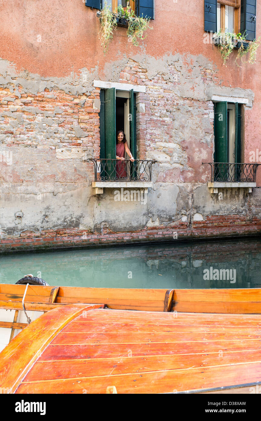 Woman Looking out of Window at a Boat Moored in Front of Old Buildings in Venice Stock Photo